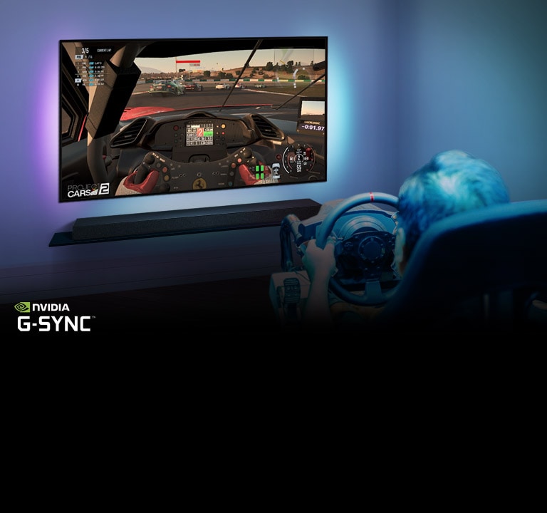 Čovek sedi u stolici za trkačku igru, drži trkački volan dok igra trkačku igru na TV ekranu