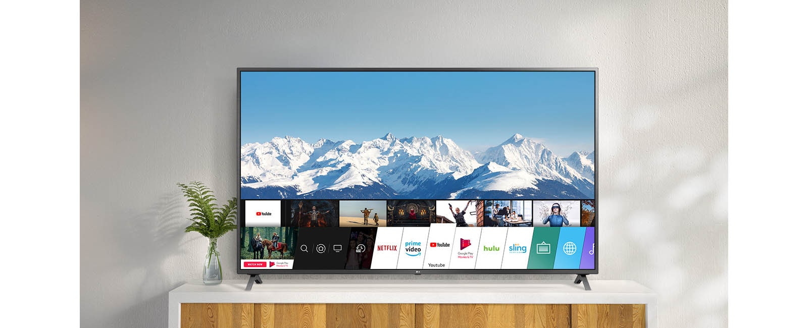 Televizor na belom postolju uz zid. Ekran televizora prikazuje početni ekran sa operativnim sistemom webOS.