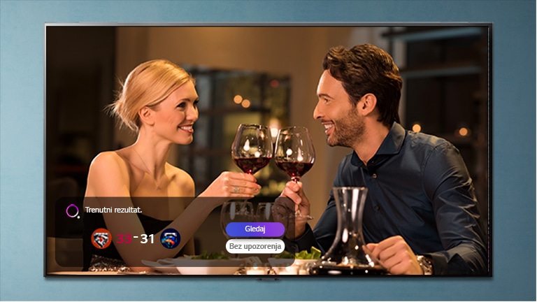 Muškarac i žena se kuckaju čašama na TV ekranu dok se prikazuje trenutni rezultat izabranog sportskog događaja