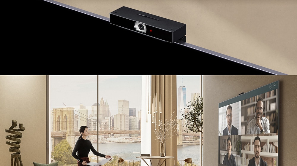 Žena sedi na sofi sa naslonom za ruke, drži laptop računar i gleda TV. Na velikom TV ekranu možete videti četiri junaka i video-konferenciju.