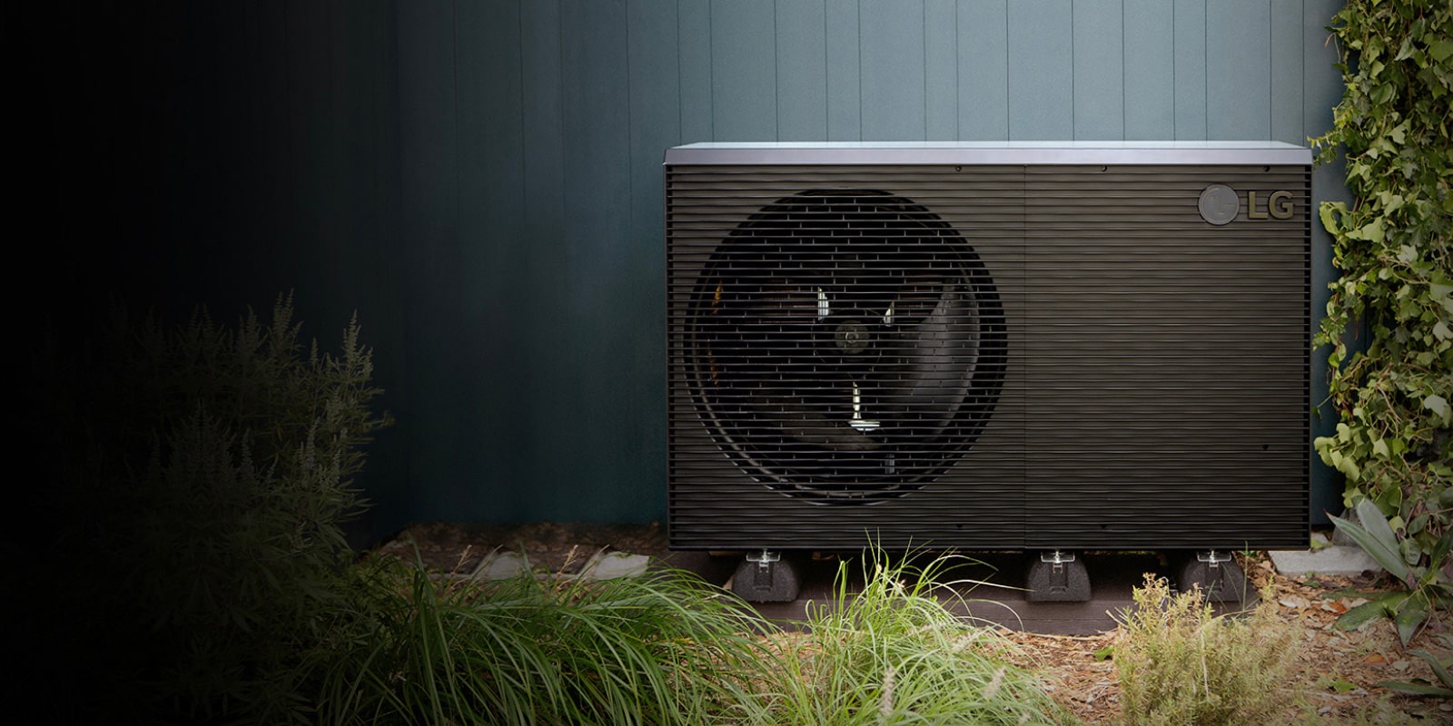 LG toplotna pumpa vazduh/voda THERMA V R290 Monoblok, spoljna jedinica crne boje stavljena je na zeleni spoljni zid kuće.