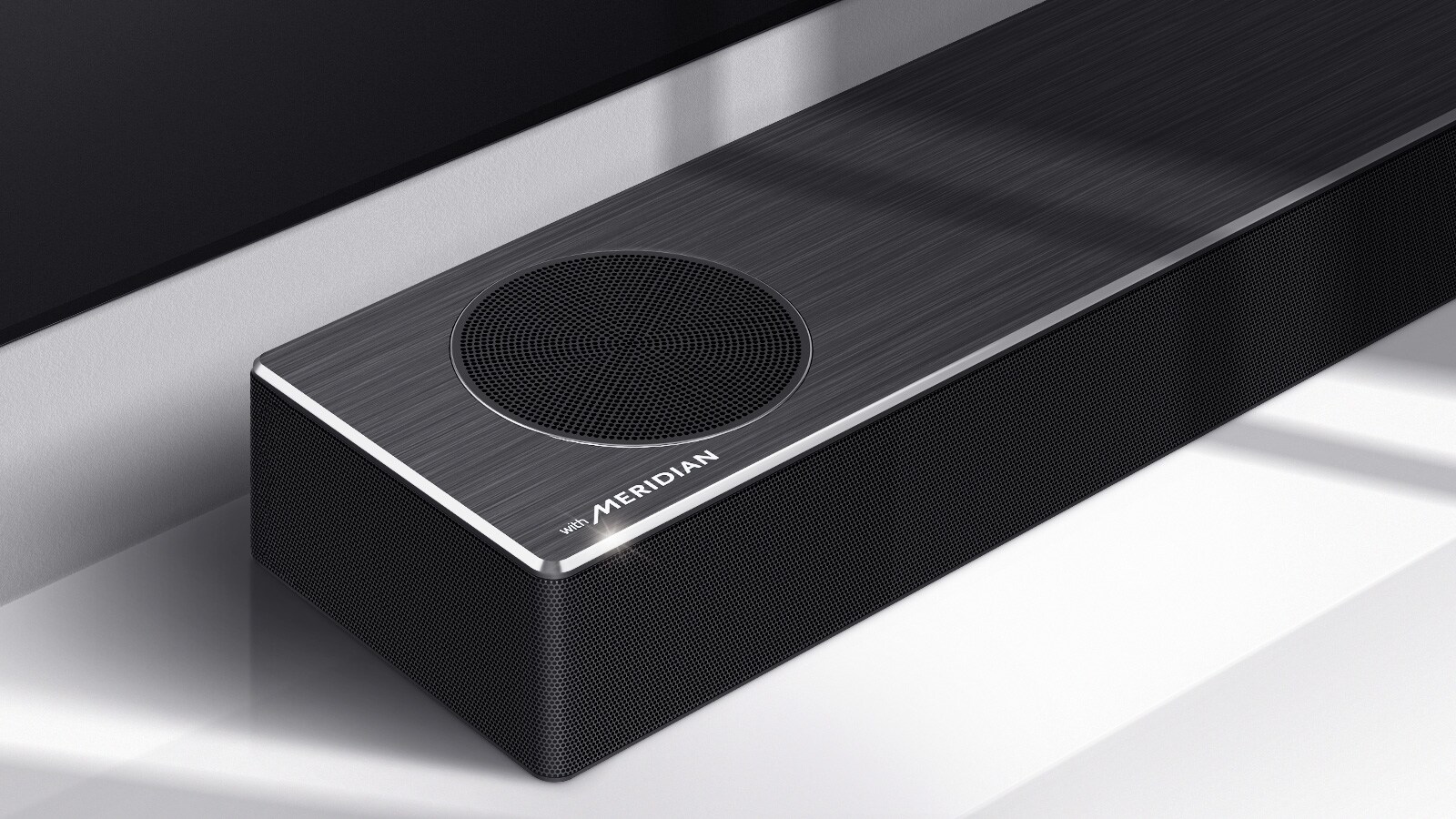 Krupan kadar leve strane LG Soundbar zvučnika sa logotipom Meridian prikazanim u donjem levom uglu proizvoda. Donja leva strana televizora je takođe vidljiva.