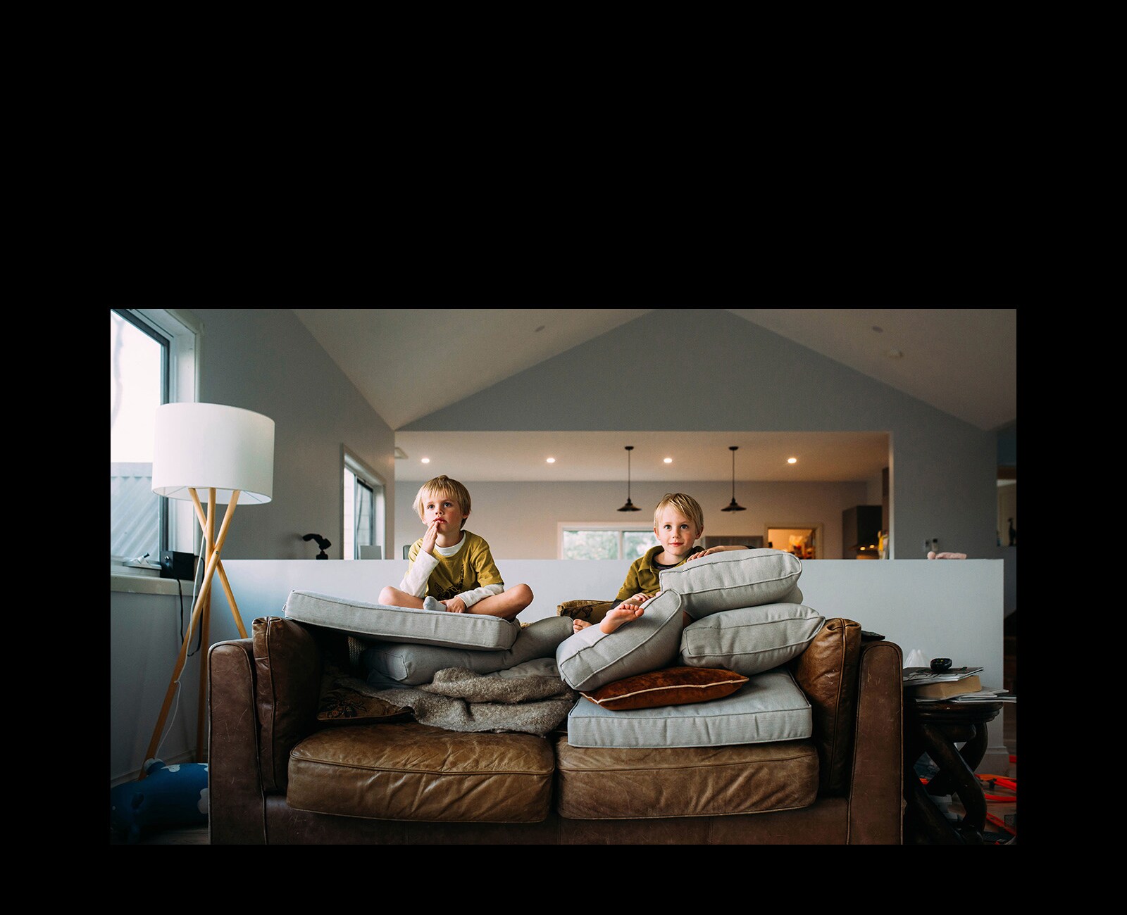 Dva dečaka blizanca gledaju nešto i sede na sofi.