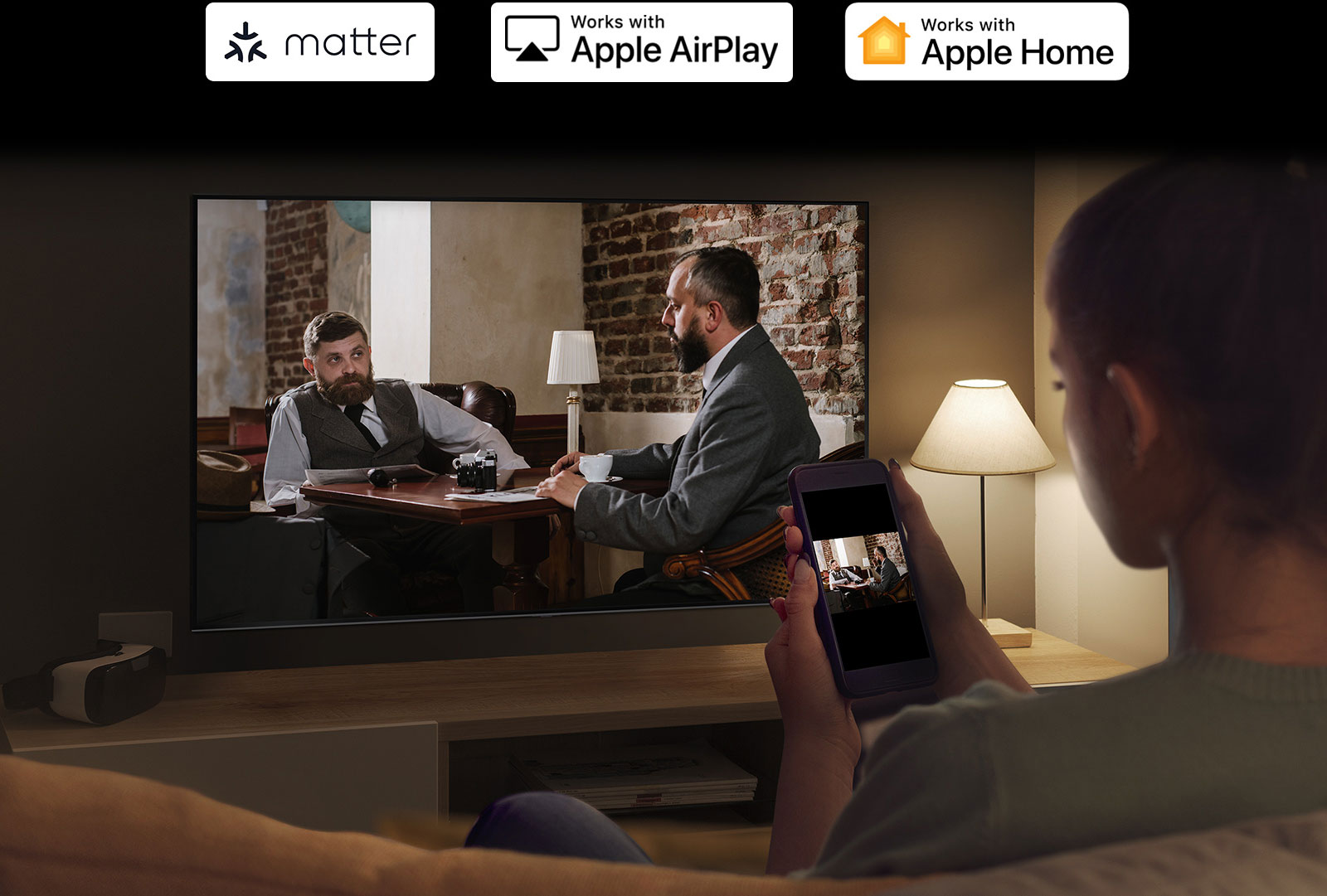 Prikazana je žena u mračnoj prostoriji koja gleda video-sadržaj sa telefona na televizoru pomoću preslikavanja.