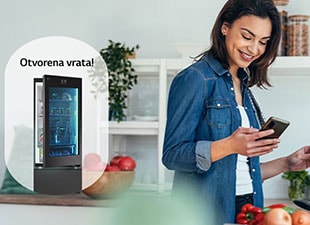 Slika žene koja prima obaveštenje na svoj pametni telefon iz aplikacije LG ThinQ o tome da su vrata frižidera ostavljena otvorena dok ona kuva.