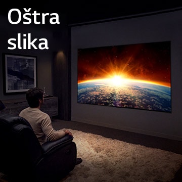 Čovek sedi na kauču u mračnoj prostoriji i gleda televizor na kome je prikazan izlazak Sunca iza Zemlje.