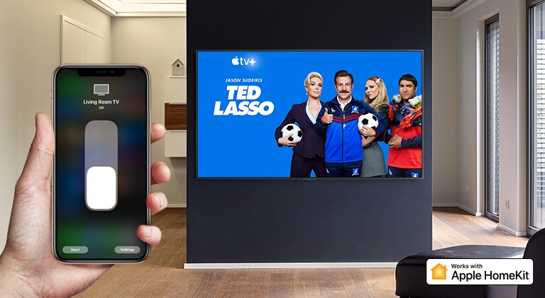 Krupan kadar ruke koje upravlja televizorom preko iPhone uređaja i televizor na kom se prikazuje sadržaj Apple TV+, Ted Lasso.