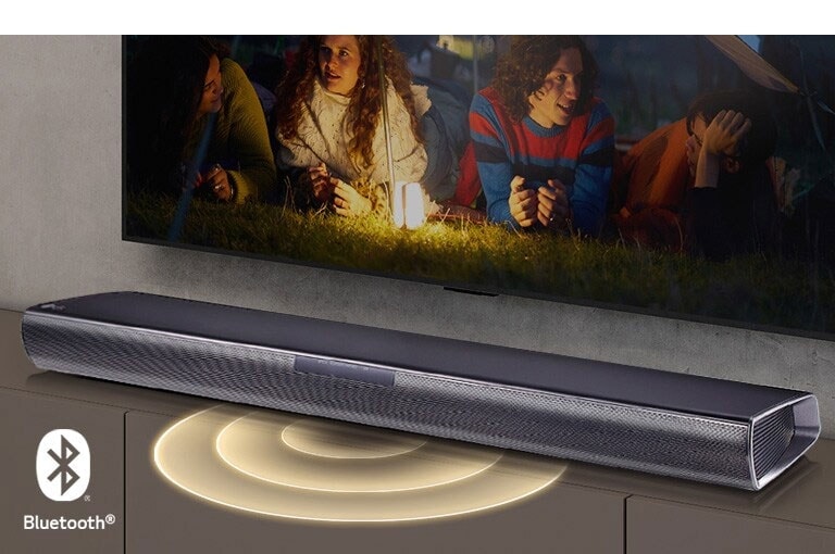 LG TV je na zidu, na ekranu se prikazuju 2 para koja leže na travi. Ispred njih se nalazi lampa. LG Soundbar zvučnik nalazi se ispod LG televizora. Grafika zvuka se pojavljuje iz prednjeg dela Soundbar zvučnika. Logotip Bluetooth prikazan je u donjem levom uglu slike.