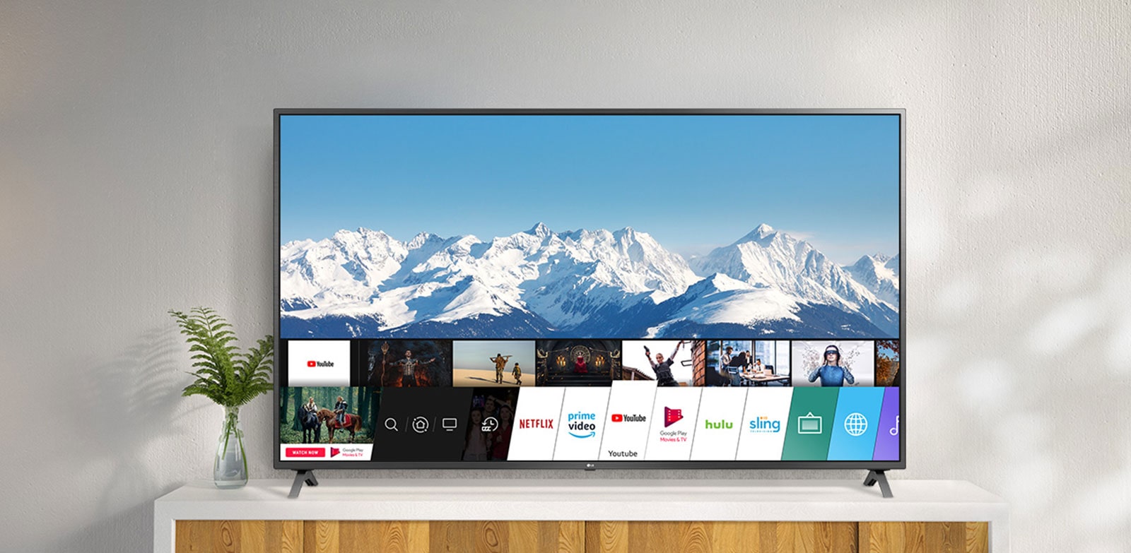 Televizor na belom postolju uz zid. Ekran televizora prikazuje početni ekran sa operativnim sistemom webOS.