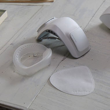 Рука держит силиконовую подушечку, а маска лежит на столе на заднем плане.