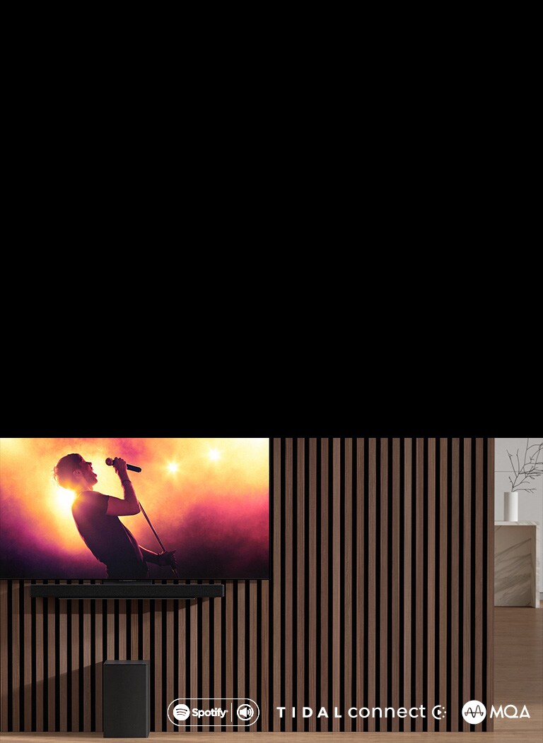 Телевизор LG OLED серии C закреплен на стене, а под ним находится саундбар LG SC9S, закрепленный с помощью эксклюзивного кронштейна. Снизу находится сабвуфер. На телевизоре демонстрируется сцена концерта.