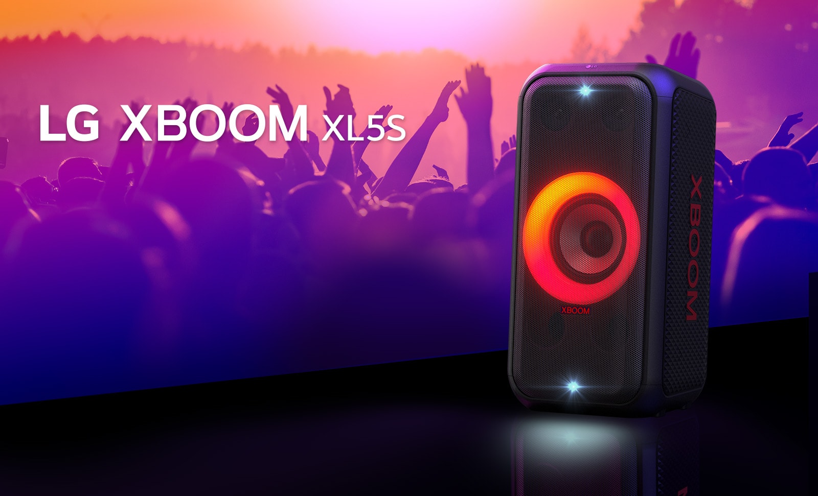 LG XBOOM XL5T стоит на сцене с включенной подсветкой с красно-оранжевым градиентом. За сценой люди наслаждаются музыкой.