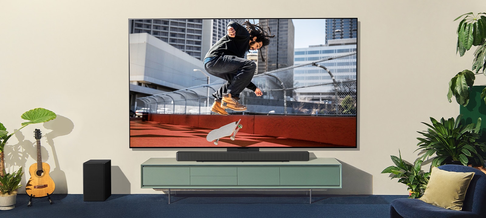 Две женщины сидят на диване перед настенным телевизором LG TV в красочной гостиной, и одна из них направляет пульт на экран телевизора. 