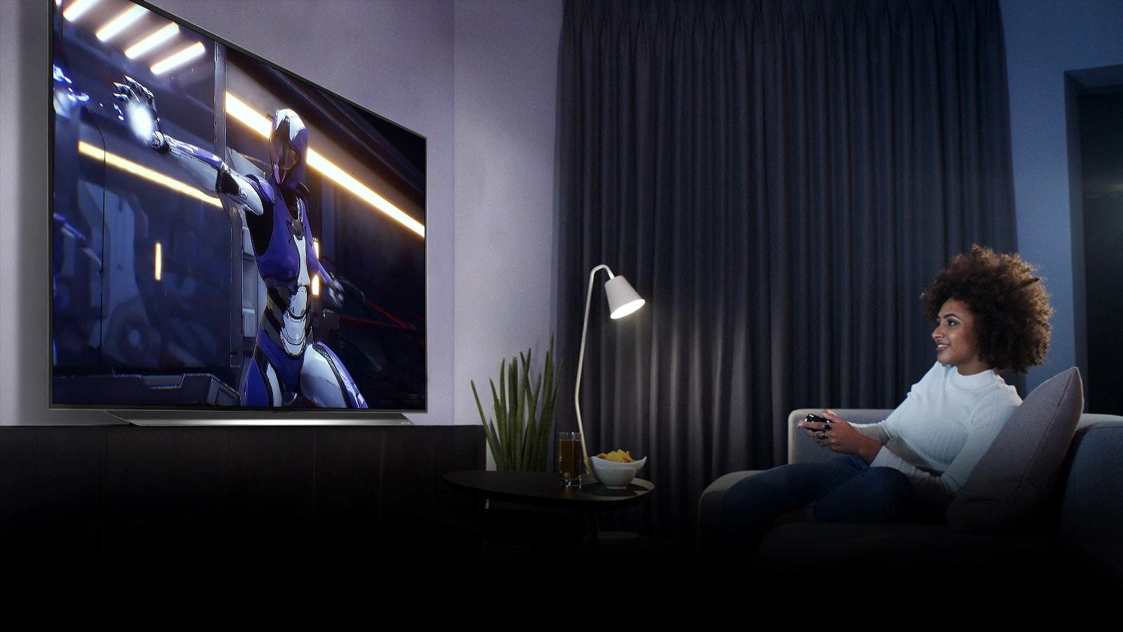 «Женщина сидит на диване, держа джойстик во время игры в игру на экране телевизора»