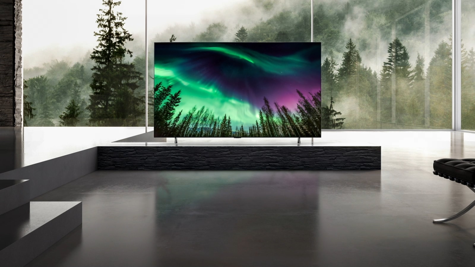 The camera moves from a close-up of the top of the TV down to a close-up of the front of the TV.  There are green northern lights on the TV screen.  The camera zooms out to reveal a spacious living room.  The living room is mostly gray and the forest is visible outside the window.