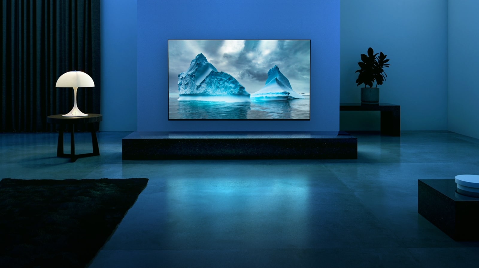 Синий неоновый контур движется по изображению синего ледника. Камера отдаляется и показывает голубой ледник на экране телевизора. Телевизор расположен в просторной гостиной с голубым фоном. 