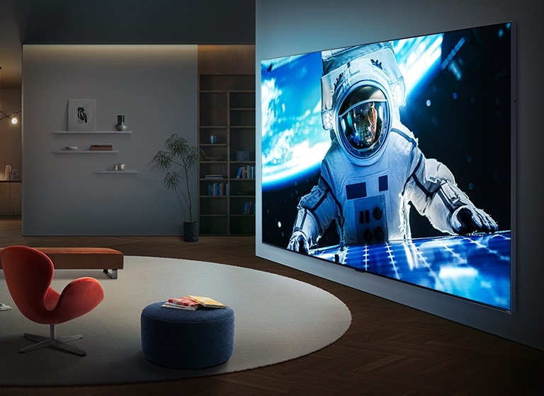 Сверхбольшой телевизор LG QNED evo AI QNED90 Mini LED закреплен на стене в современной гостиной, отображая на широком экране крупномасштабную сцену с астронавтом, которая визуально заполняет комнату и создает сильный кинематографический эффект.