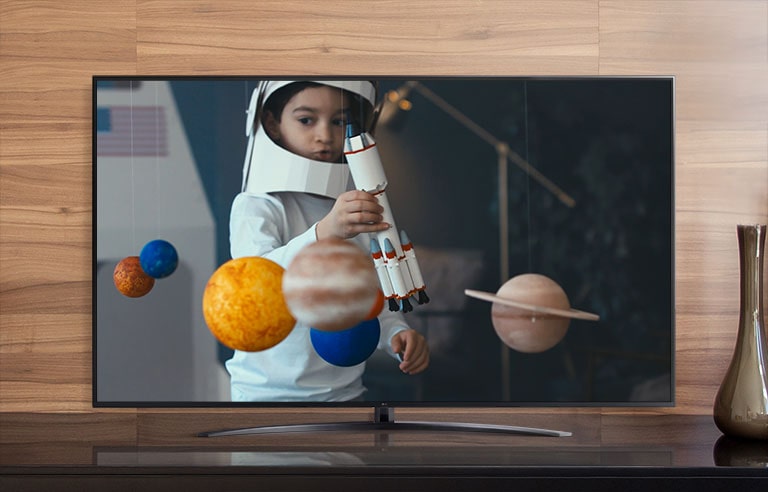 Экран телевизора с мальчиком в самодельном костюме космонавта, играющим с космическим кораблем в комнате, украшенной миниатюрами планет (просмотр видео)