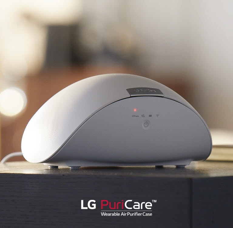 Футляр для носимого очистителя воздуха LG PuriCare стоит на столе. На дисплее горит красный свет.