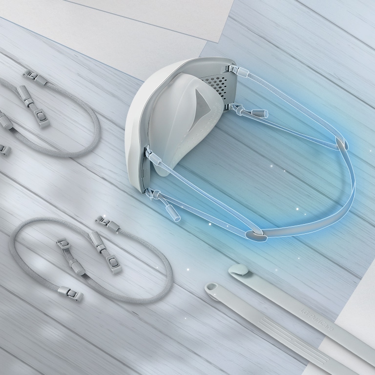 Верх и внутренняя часть маски показаны с эластичной тканевой лентой, соединенной сзади и выделенной синим цветом. На столе вокруг маски лежат дополнительные эластичные тканевые ленты.