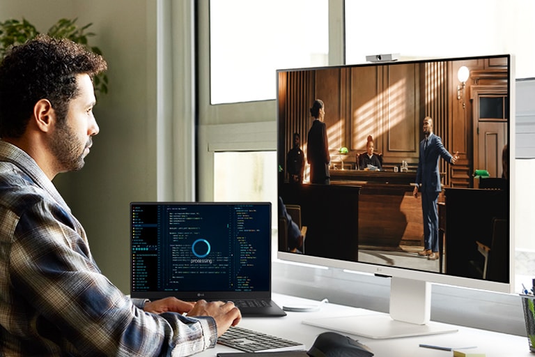 Мужчина наслаждается стриминговым контентом на мониторе LG MyView Smart Monitor в ожидании завершения выполнения задач на ноутбуке.