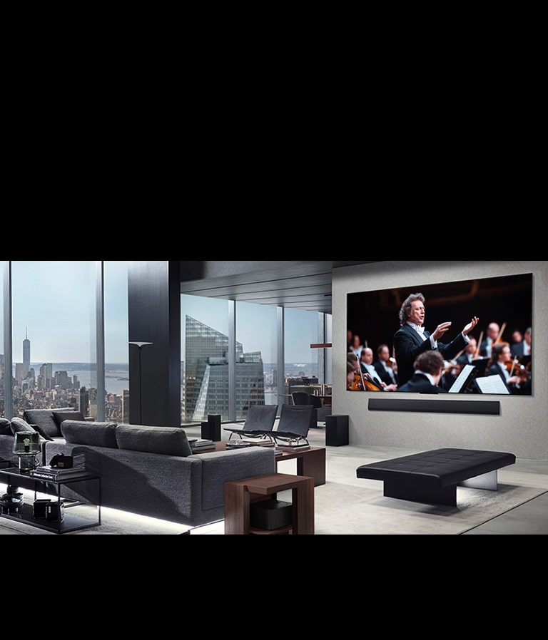 Гостиная с LG OLED TV и звуковой панелью LG Soundbar, установленными на стене. Приставка для нулевого подключения едва заметна под боковым столиком рядом с диваном, что показывает, как легко ее можно разместить в любом месте. Вся планировка гостиной выглядит аккуратно и опрятно.