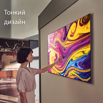 Женщина смотрит закрепленный на стене телевизор, на котором демонстрируется живопись.