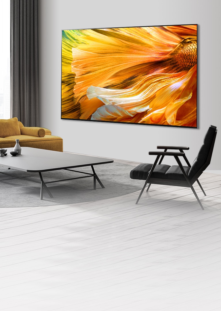 Изображение телевизора LG QNED MiniLED с большим экраном, закрепленного на серой стене.  Перед телевизором расставлены диван, журнальный столик и стулья.