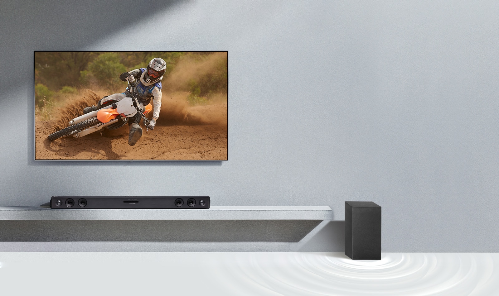 Саундбар LG SQC2 и телевизор LG в гостиной. Рядом с саундбаром находится сабвуфер. Телевизор включен, на экране демонстрируется изображение мотоцикла.