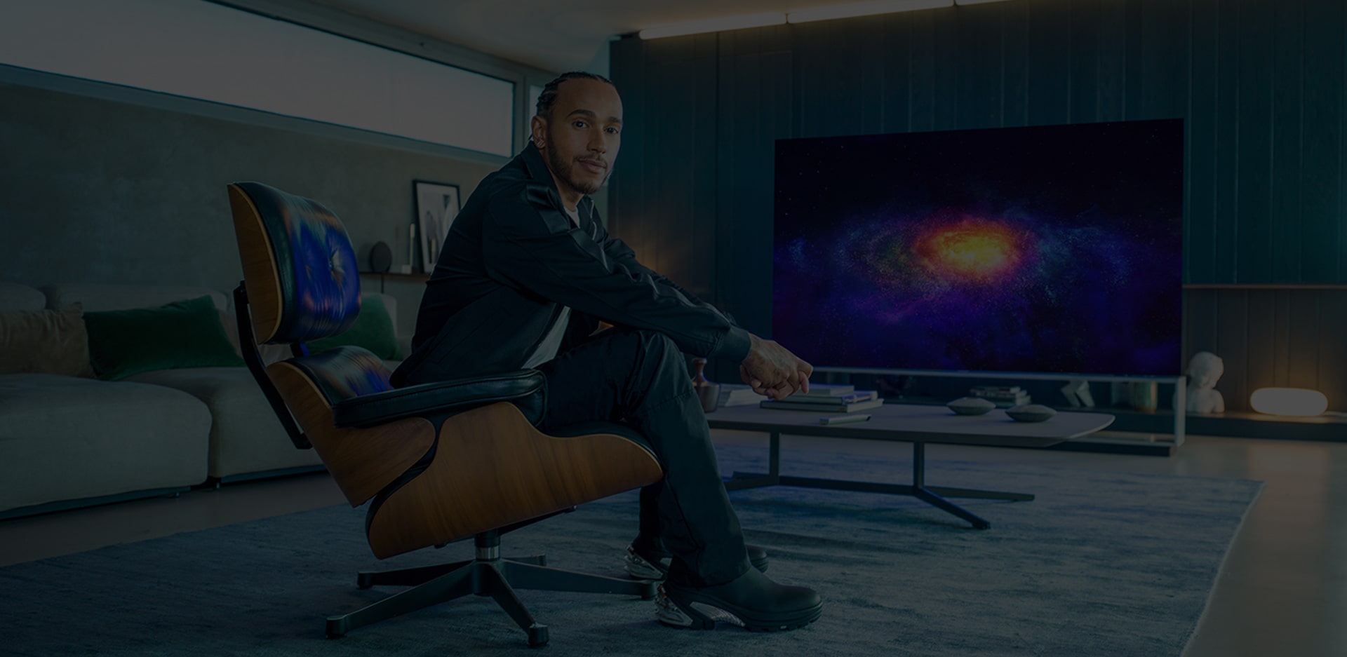 Льюис Хэмилтон сидит в кресле напротив телевизора LG SIGNATURE OLED 8K.