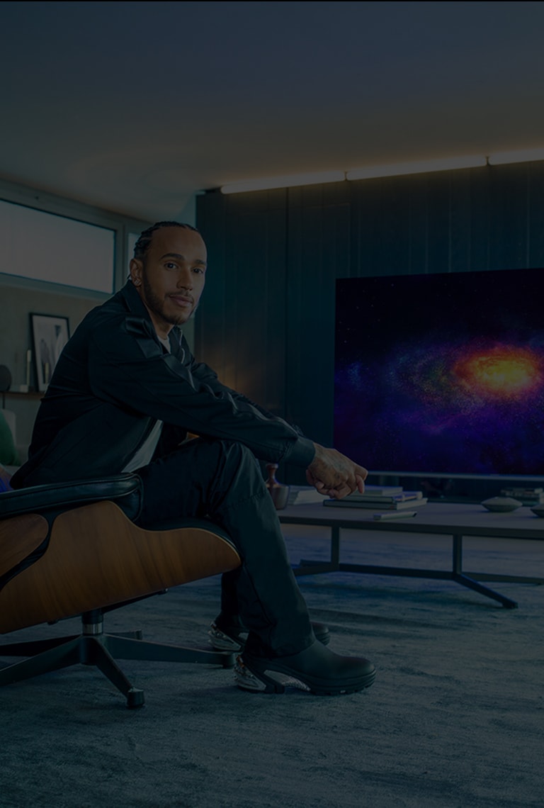 Льюис Хэмилтон сидит в кресле напротив телевизора LG SIGNATURE OLED 8K.