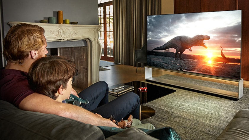 Father and son watching a dinosaur documentary on a large screen TV