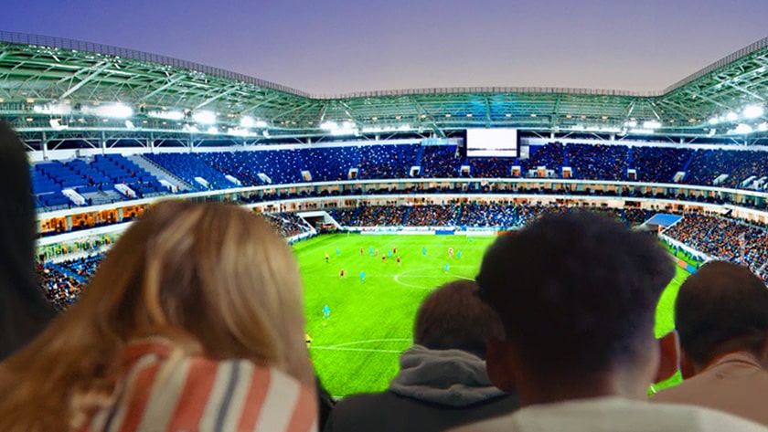 People are watching a football game with the backdrop of a view of the entire stadium on a large TV