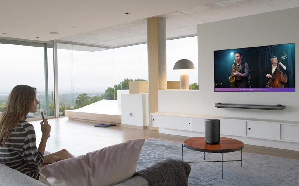 A woman sitting in her living room, using her LG remote control to speak to her LG OLED Wallpaper TV. 