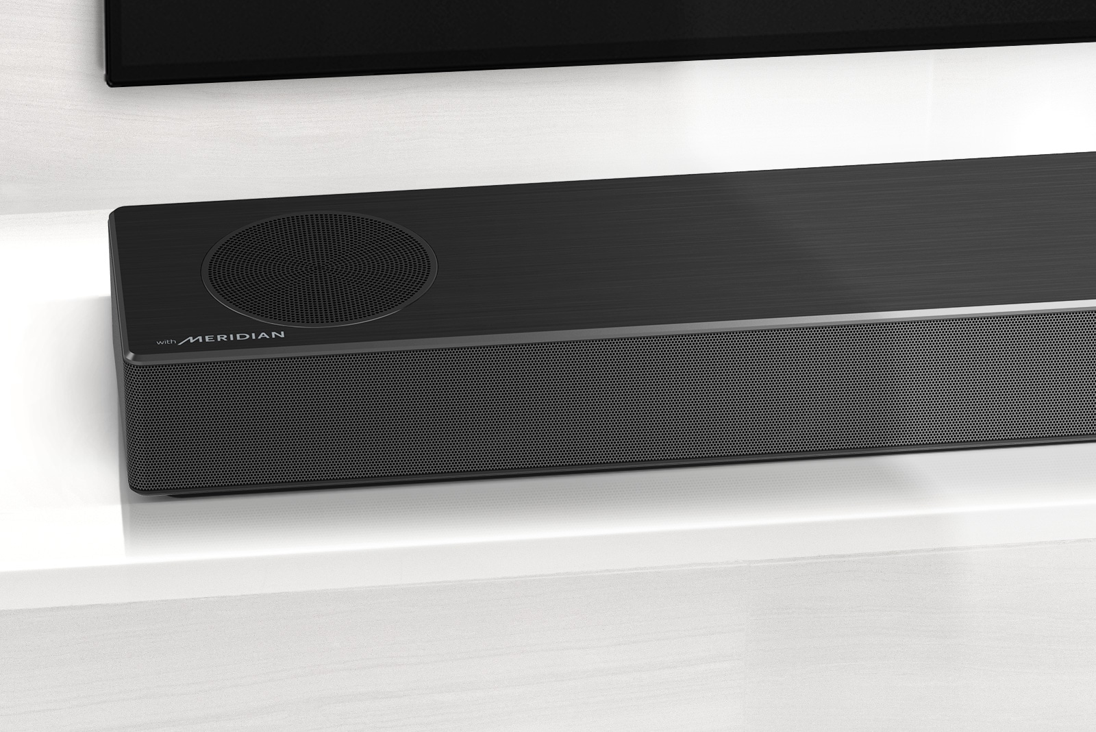Detailný pohľad na ľavú stranu LG Sound Baru s logom Meridian, ktoré je zobrazené v ľavom dolnom rohu. Vidieť aj ľavú dolnú časť televízora.