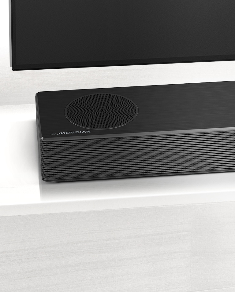 Detailný pohľad na ľavú stranu LG Sound Baru s logom Meridian, ktoré je zobrazené v ľavom dolnom rohu. Vidieť aj ľavú dolnú časť televízora.