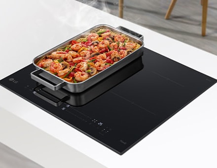 Na dvoch horákoch na indukčnej varnej doske sa nachádza široká panvica. Z jedla na panvici vychádza para.