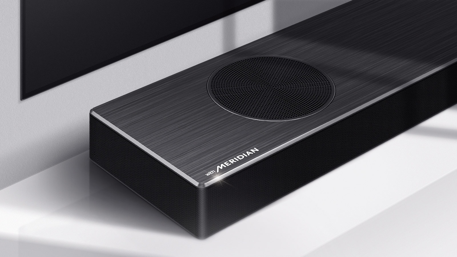 Detailný pohľad na ľavú stranu Soundbaru LG s logom Meridian, ktoré je zobrazené v ľavom dolnom rohu produktu. Vidieť aj ľavú dolnú časť televízora.