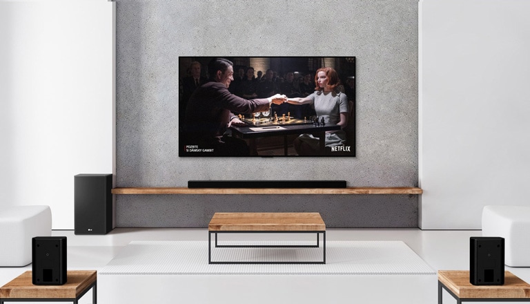 Konfigurácia s 2 zadnými reproduktormi, subwooferom, zvukovým panelom a televízorom v bielej obývačke.  Na televíznej obrazovke je žena hrajúca šach s mužom.