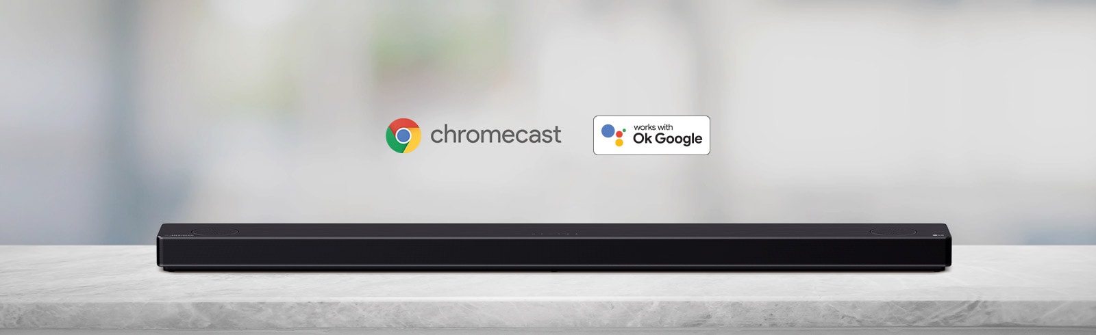 Na sivej polici je položený zvukový panel. Zľava doprava sú zobrazené logá platforiem AI v poradí: Chromecast a OK Google.