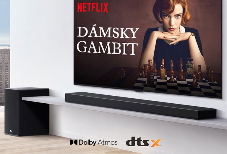 TV je umiestnený na stene.  Na televíznej obrazovke sa zobrazuje plagát televízneho programu. Zvukový panel LG sa nachádza priamo pod TV na bielej poličke a hneď vedľa neho je biely subwoofer. Logo Dolby Atmos a logo DTS:X zobrazené v strede spodnej časti obrázka.