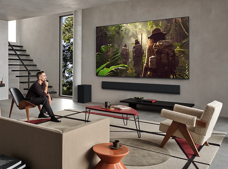 Široký záber na obývaciu izbu v luxusnom dome, kde dvojica sleduje film na televízore LG OLED TV pripevnenom na stene. Dizajn televízora elegantne splýva so stenou a interiérom.