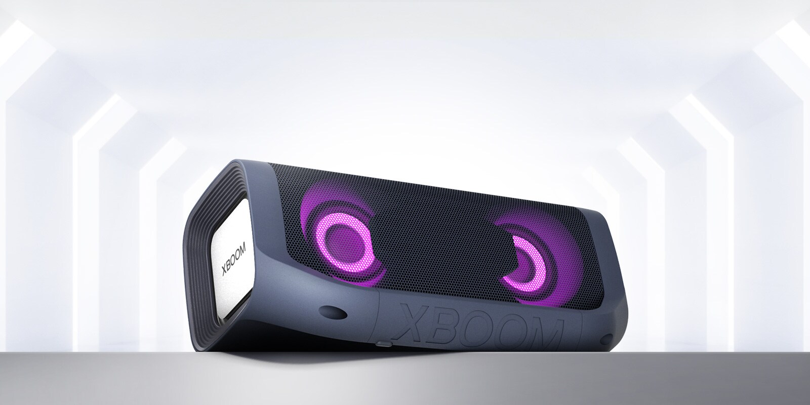 Pohľad z uhla na reproduktor LG XBOOM Go s purpurovým osvetlením položený na sivej polici.
