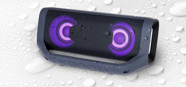 Na bielom pozadí je zobrazený reproduktor LG XBOOM Go otočený vľavo hore. Na reproduktore a pod ním sú kvapky vody.