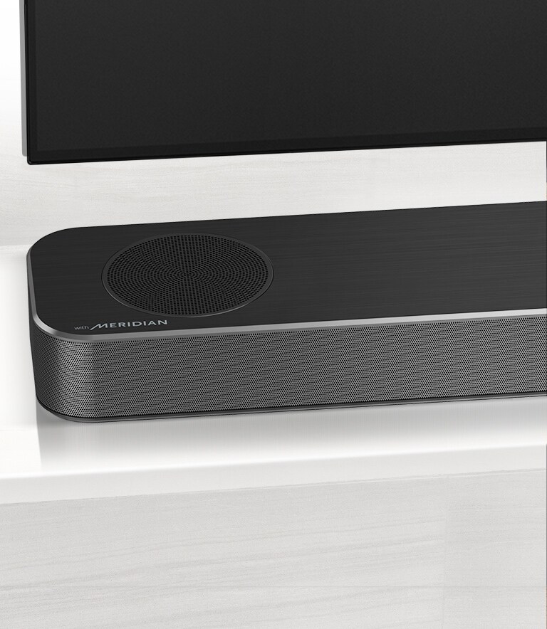 Detailný pohľad na ľavú stranu LG Sound Baru s logom Meridian, ktoré je zobrazené v ľavom dolnom rohu. Vidieť aj ľavú dolnú časť televízora.