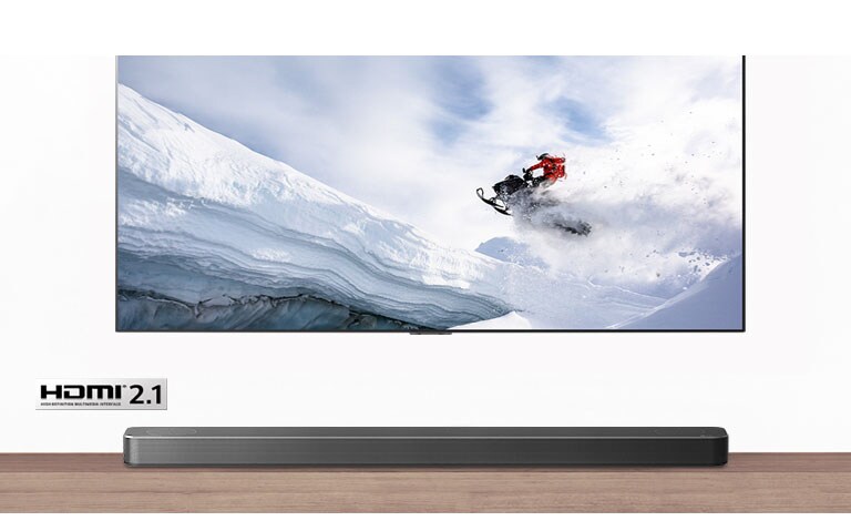 Televízor a soundbar v pohľade spredu. V televízore ide muž na snežnom skútry zasneženými horami. Logo HDMI 2.1 je pod televízorom.