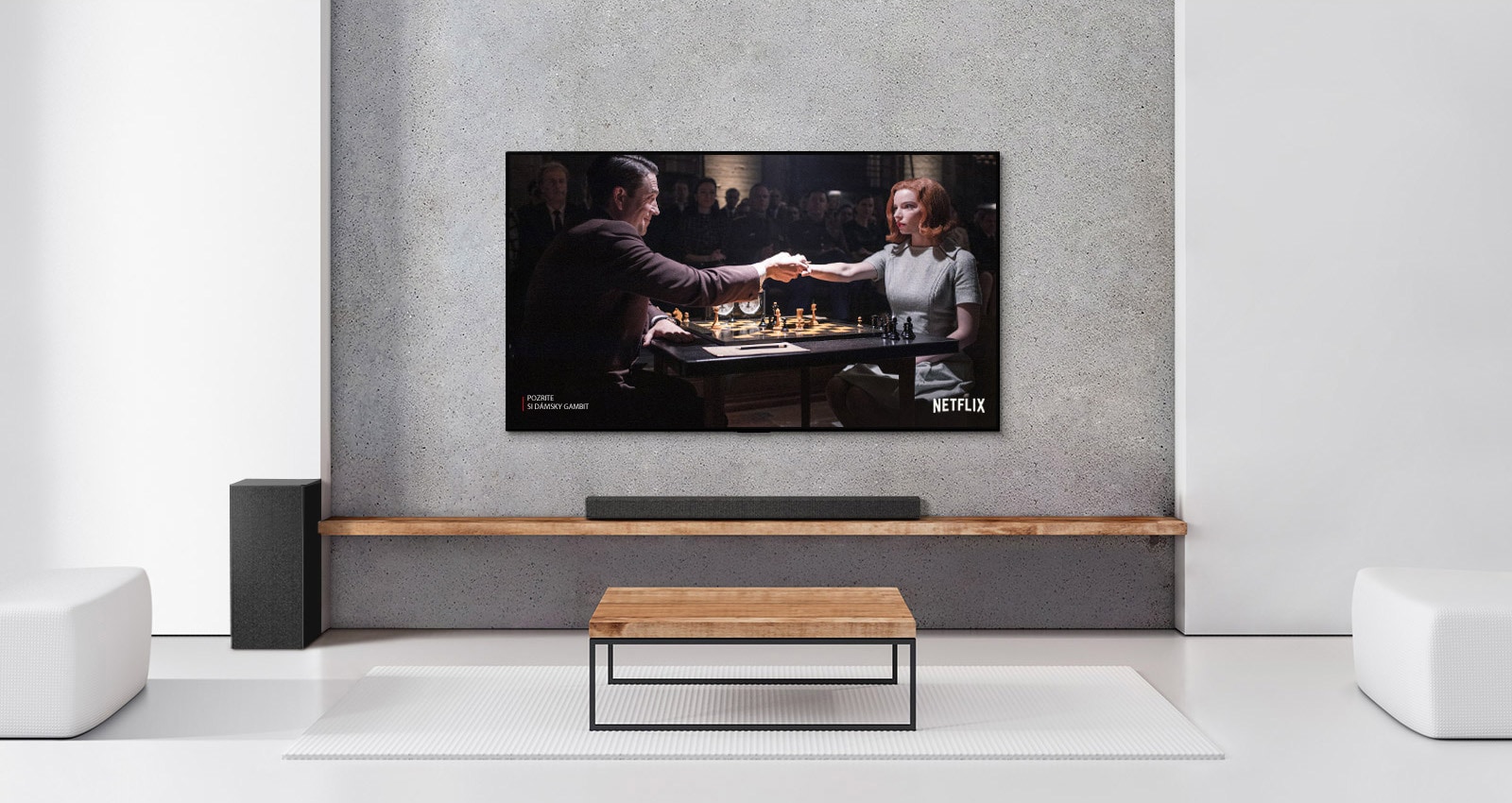 Subwoofer, Soundbarl a TV v bielej obývačke. Na televíznej obrazovke je žena hrajúca šach s mužom.