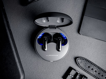 Čierne slúchadlá LG TONE Free sú položené na povrchu a medzi predmetmi (laptopmi, hodinami atď.) s rôznymi odtieňmi čiernej.