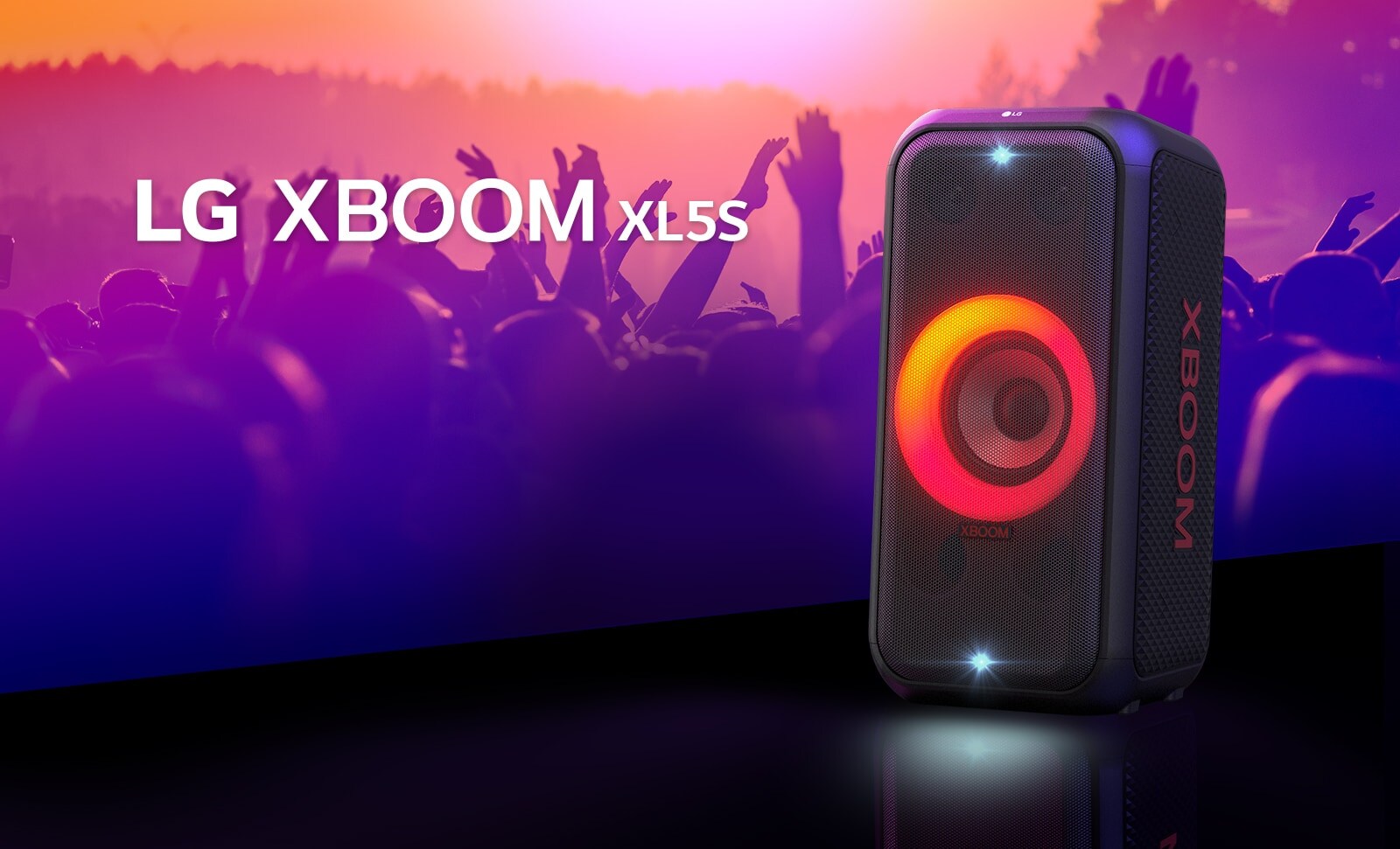 LG XBOOM XL5S umiestnený na pódiu so zapnutým červeno-oranžovým osvetlením. Za pódiom si ľudia užívajú hudbu.