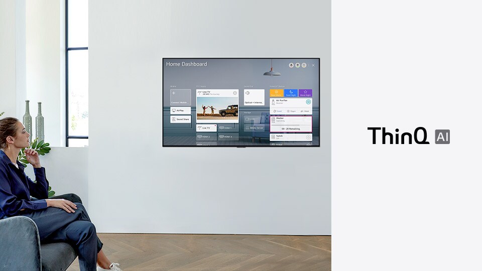 Woman sitting on a chair in the living room with the Home Dashboard on the TV screen